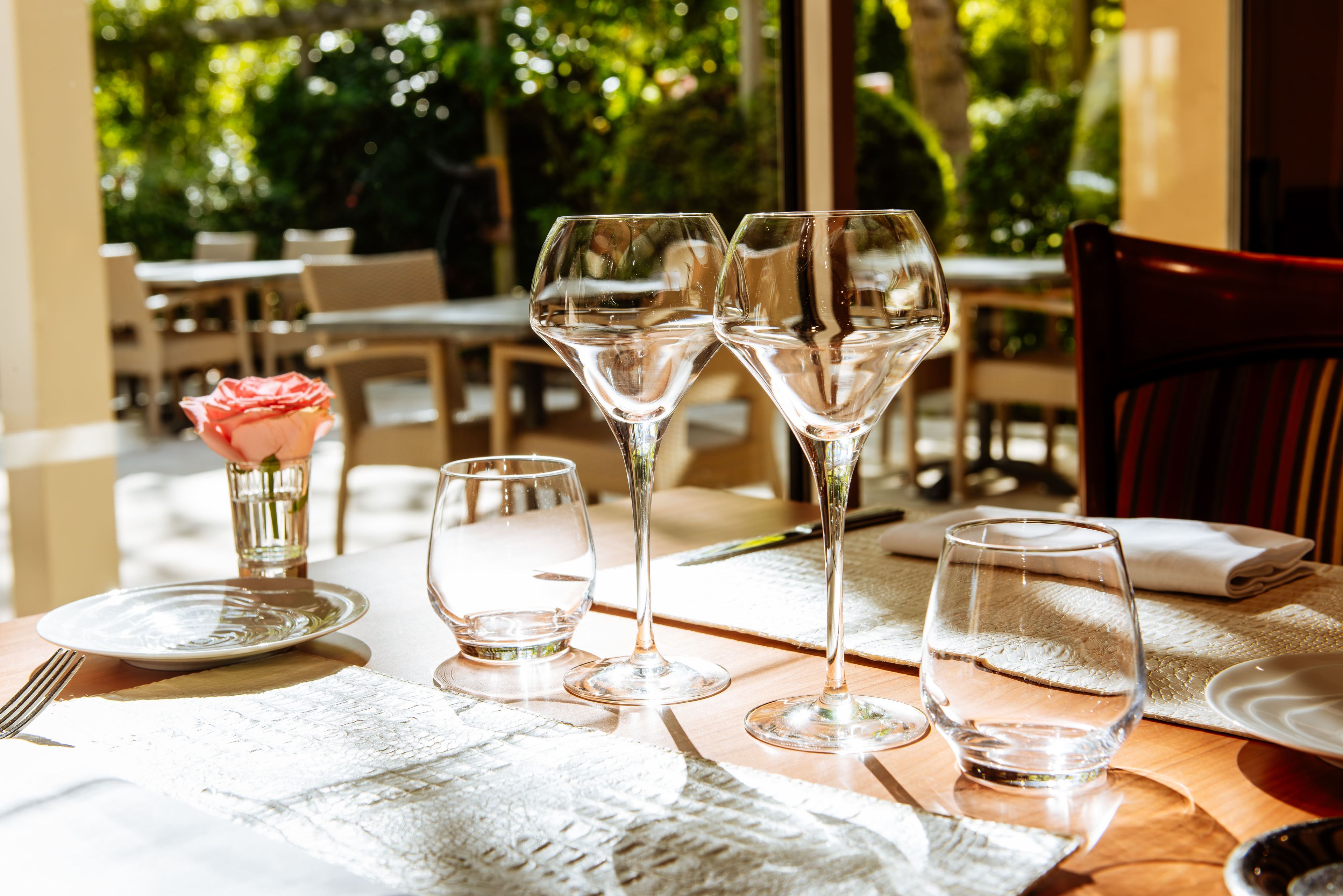 A table set with wine glasses, a rose vase, and plates, suggesting a dining area.