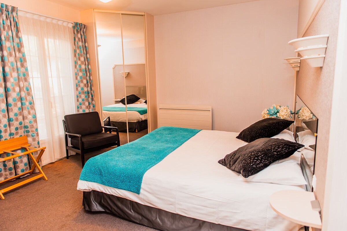 A hotel room with a bed, a chair, a desk, a mirror, and a small table.