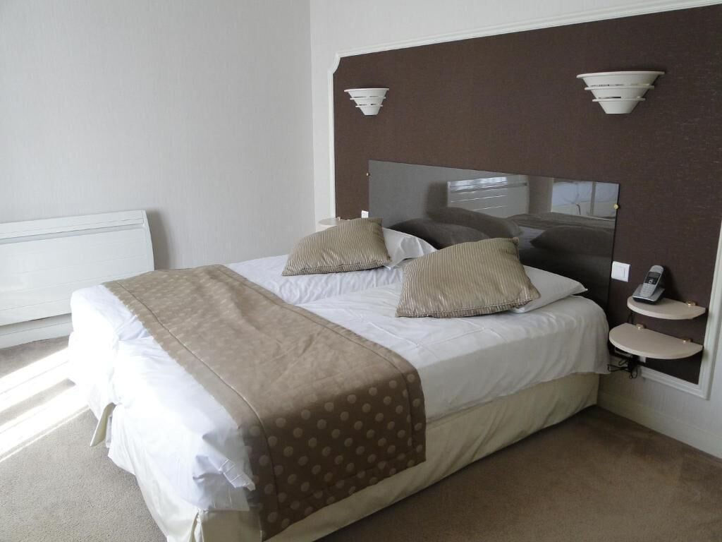 A hotel room with a bed, two bedside tables, a nightstand, a mirror, and a wall-mounted light fixture.