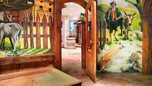 Un intérieur rustique avec des poutres en bois, un mur en pierre et une fresque représentant une scène pastorale avec un homme et des animaux.