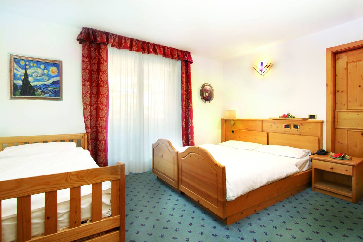 Ein Schlafzimmer mit zwei hölzernen Betten, einem Nachttisch, einer Kommode, einem Gemälde und einem Fenster mit Vorhängen.