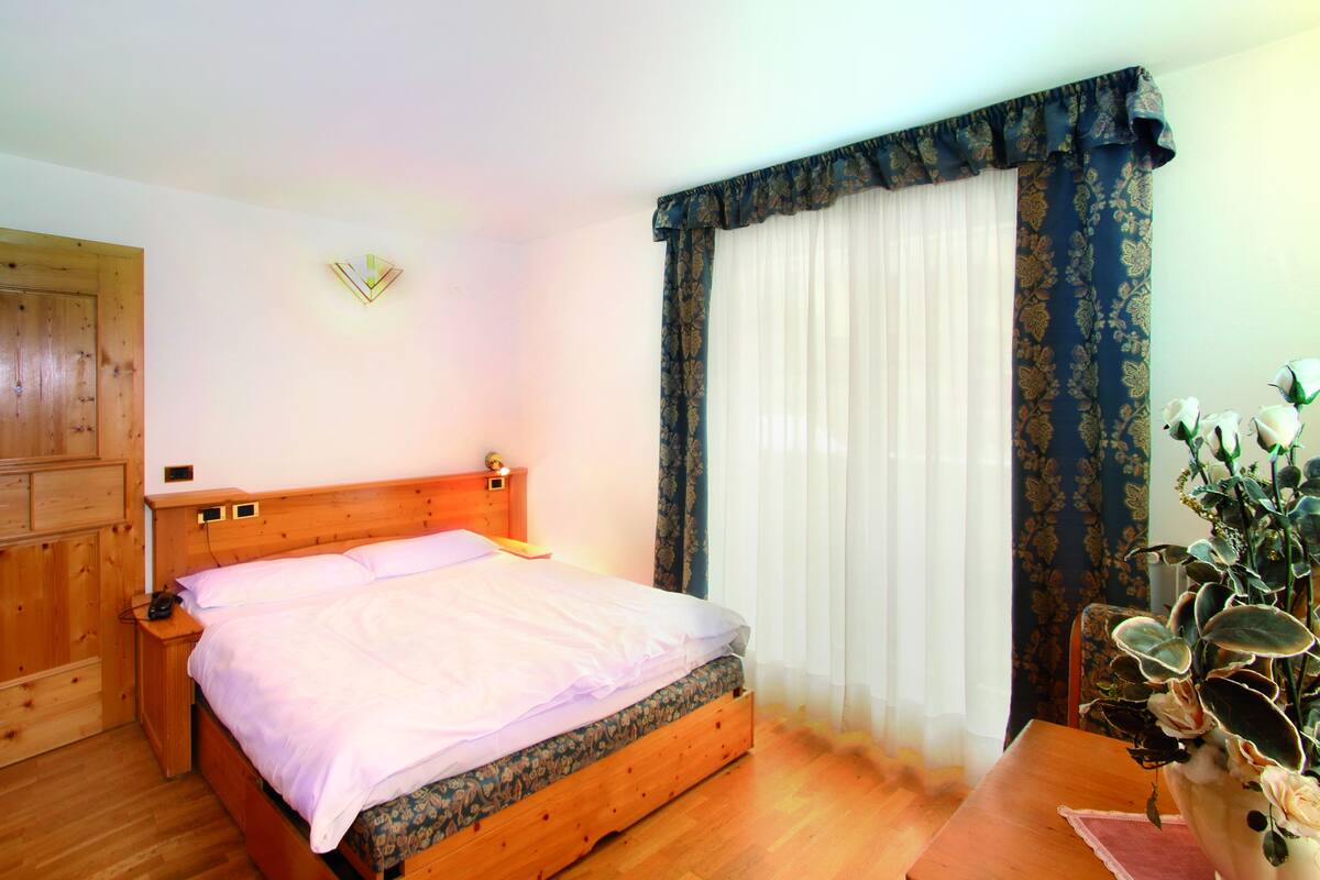 Ein Schlafzimmer mit einem hölzernen Bett, einem Nachttisch, einer Wandleuchte und einem Fenster mit Vorhängen.