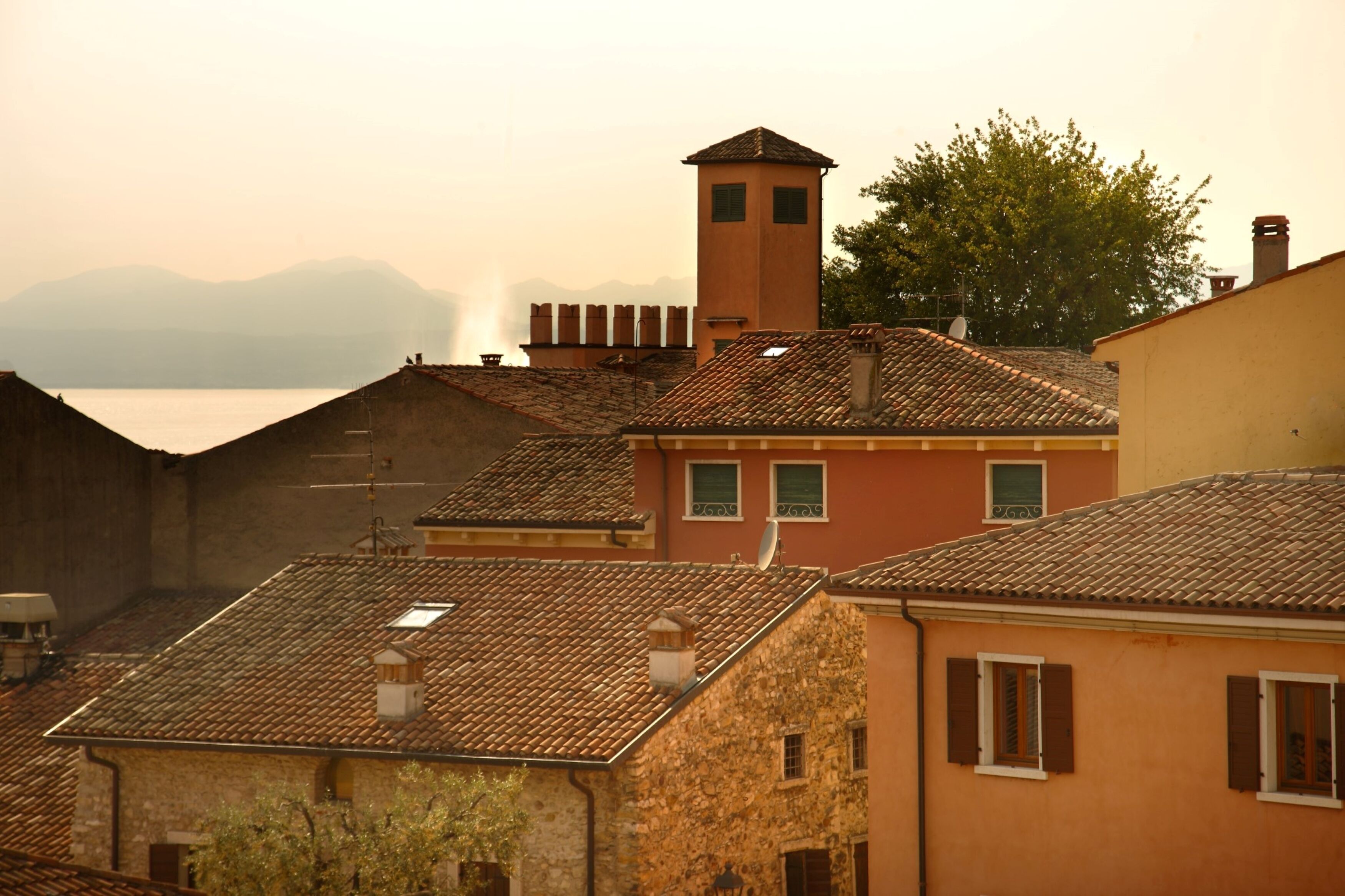 A coastal town with terracotta-roofed buildings, a prominent tower, and a view of the sea.