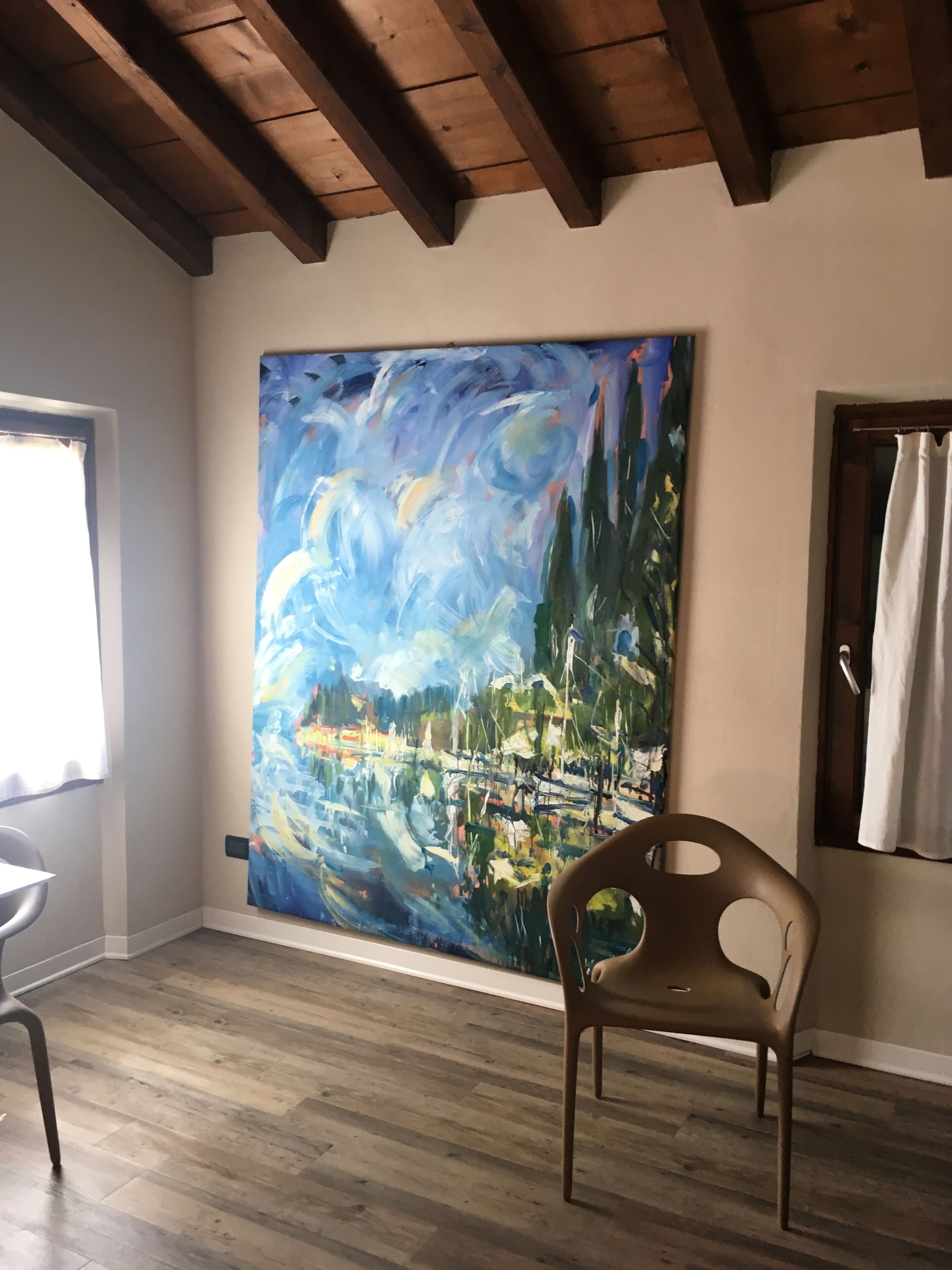 A room with a wooden ceiling, a large abstract painting on the wall, a chair, and a window.