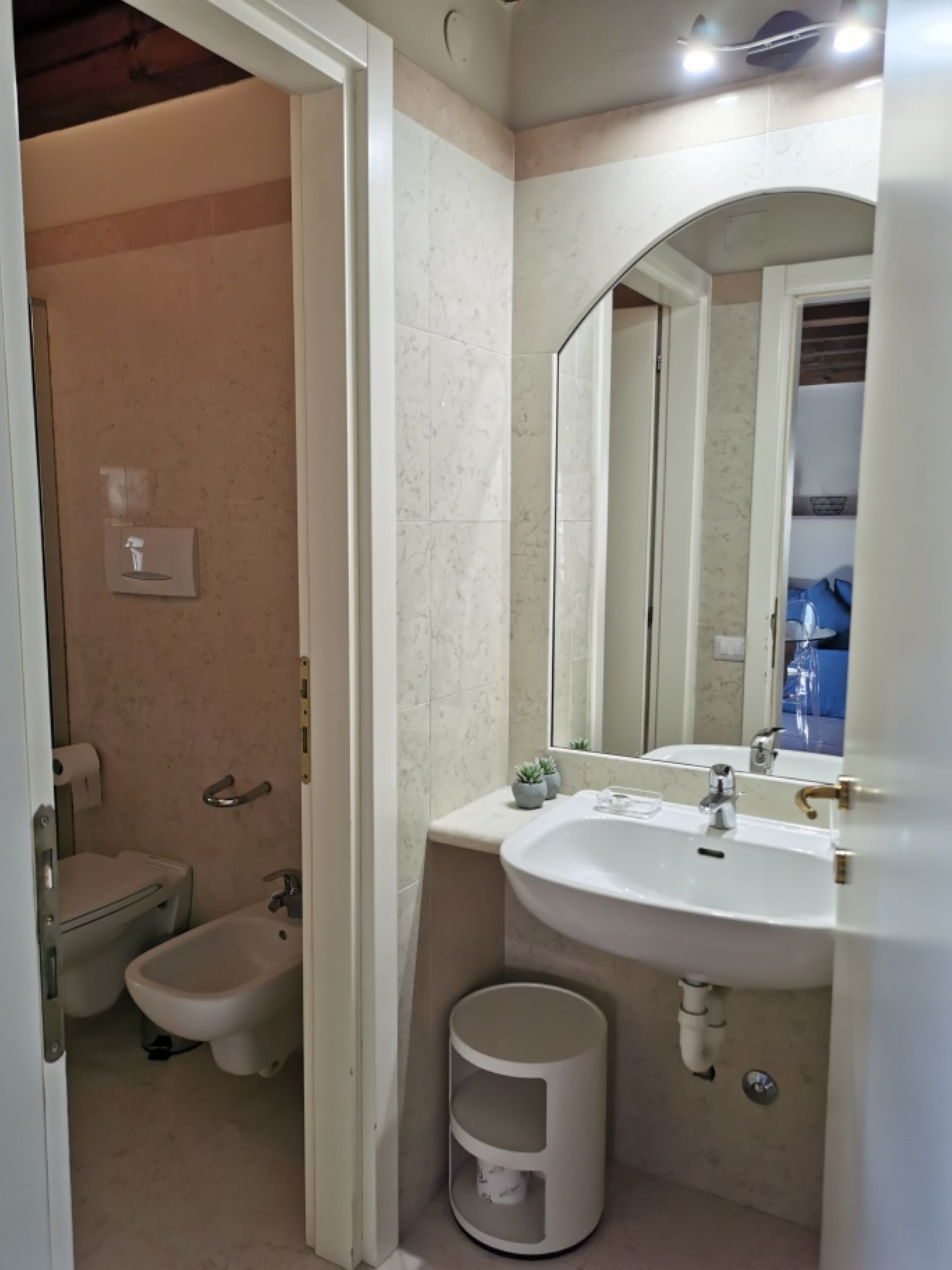 Un baño con inodoro, bidé, lavamanos, espejo y un pequeño cubo de basura.