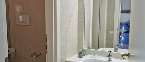 Un baño con inodoro, bidé, lavamanos, espejo y un pequeño cubo de basura.