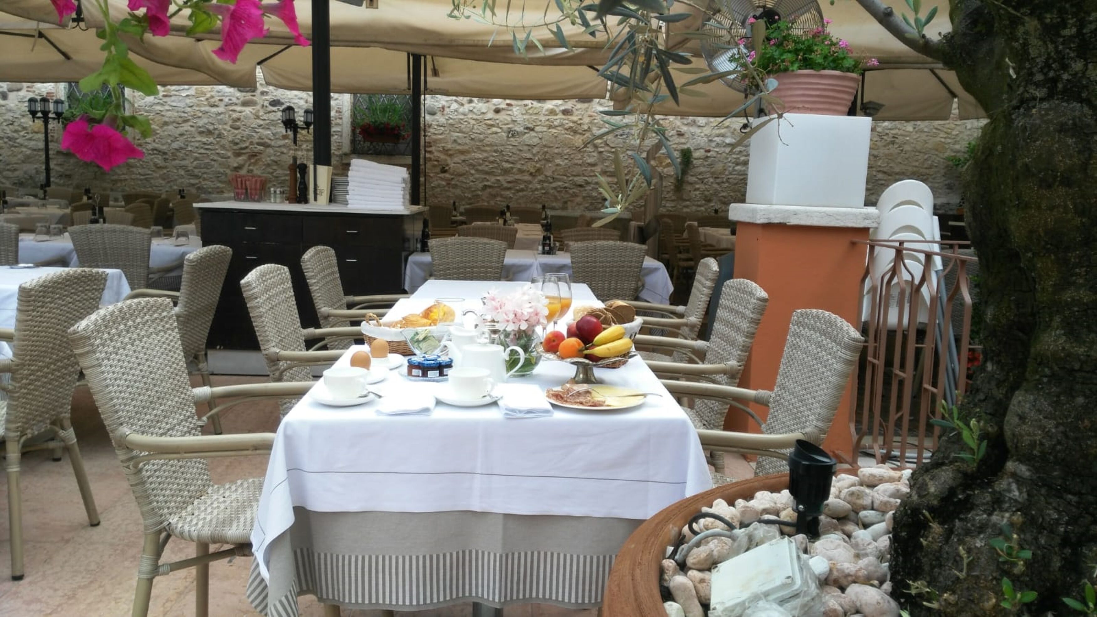 An outdoor dining area with wicker chairs and a table set for breakfast.