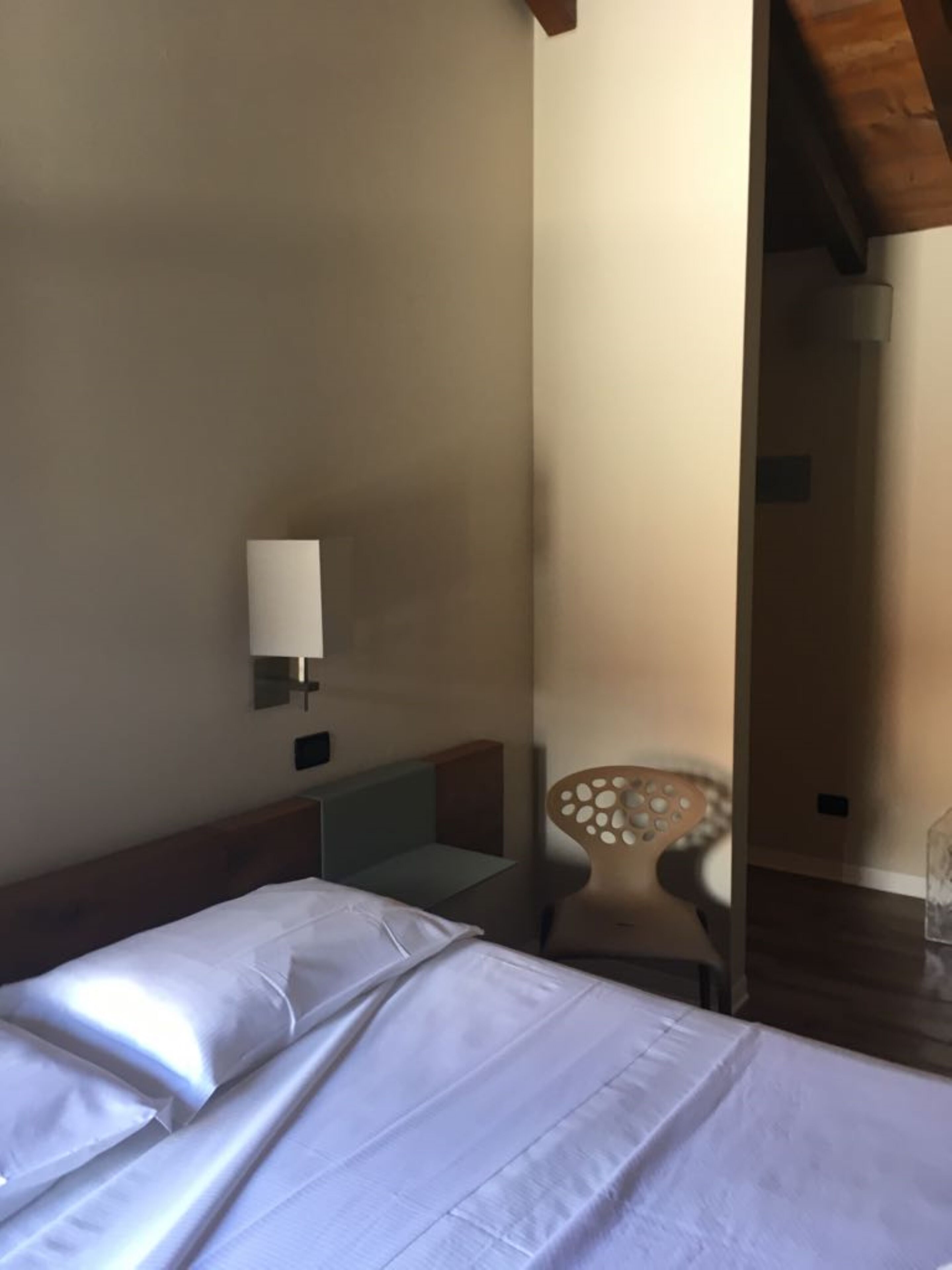 A hotel room with a bed, a nightstand, a lamp, and a chair.