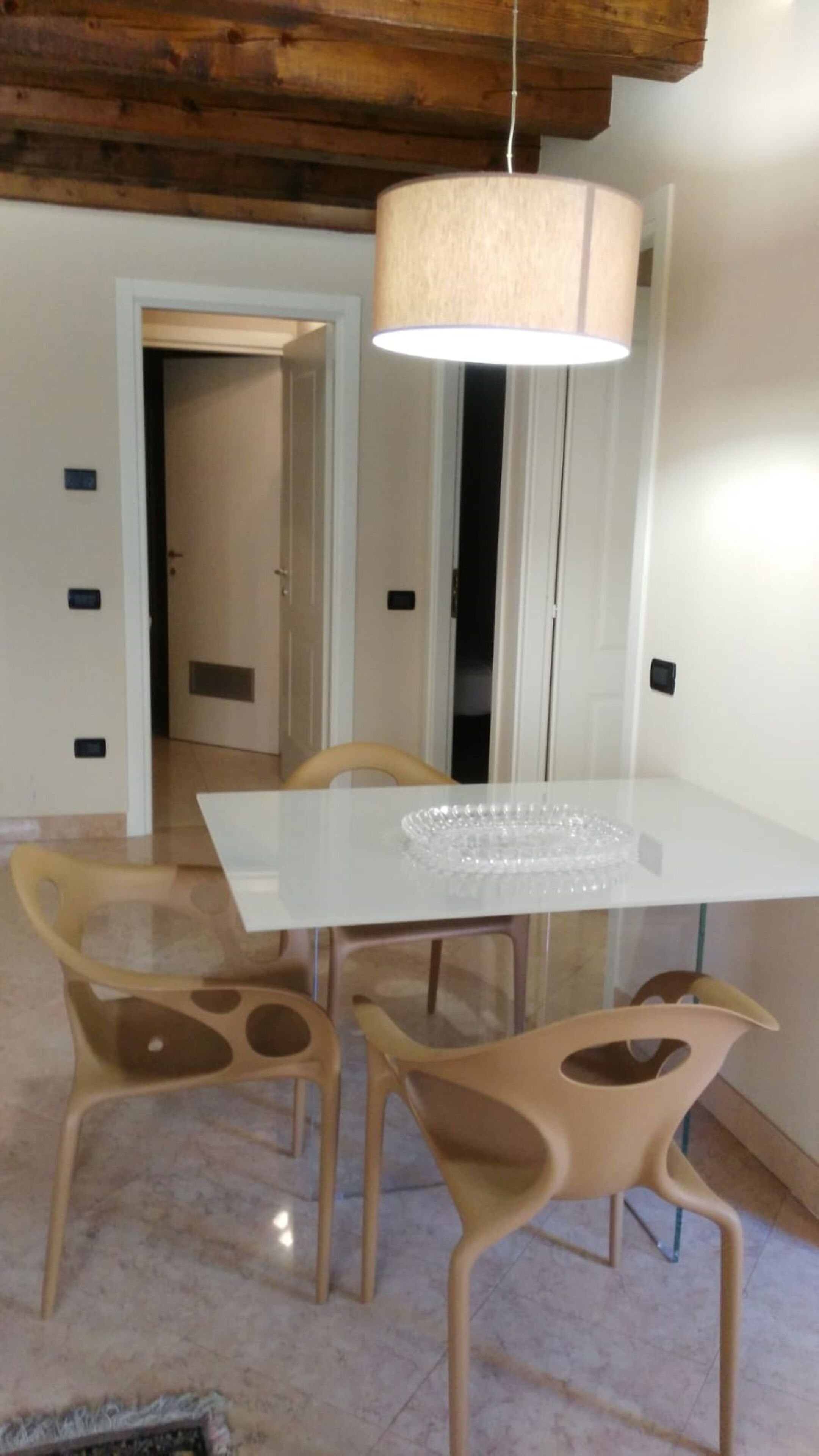 A dining area with a white table, four beige chairs, and a hanging light fixture.