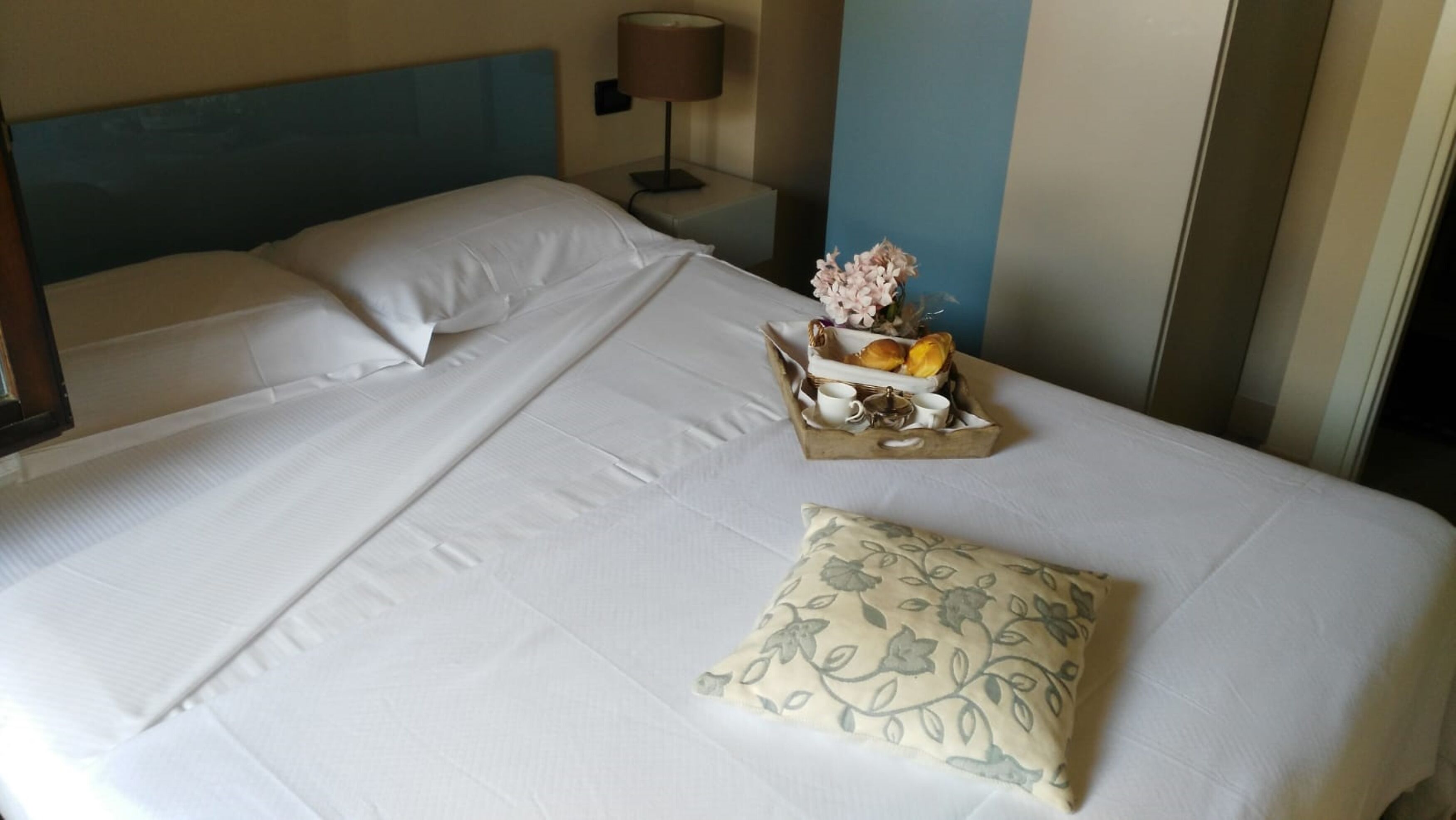 A neatly made bed with white linens, a floral pillow, and a tray with breakfast items.