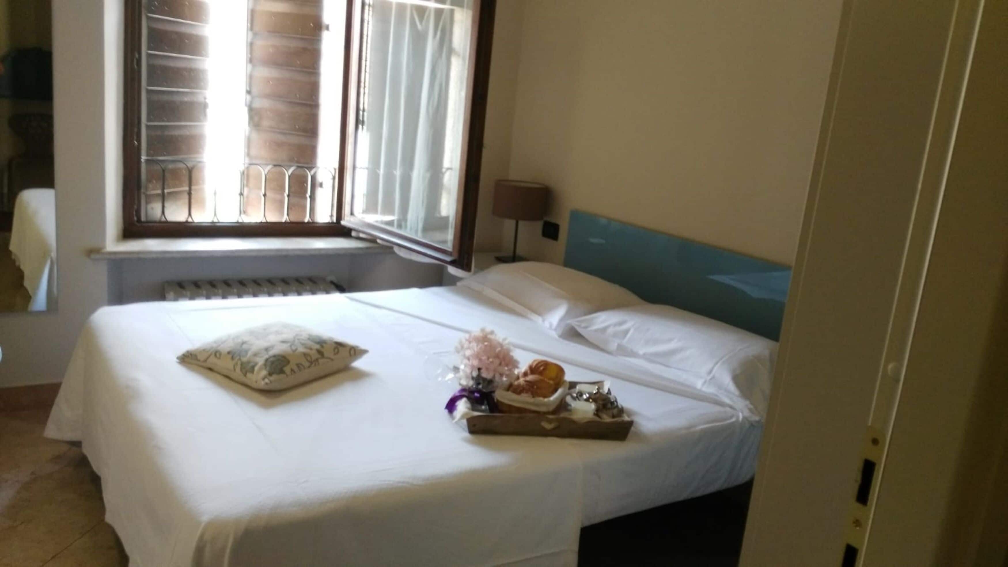 Ein Hotelzimmer mit Bett, Fenster mit Jalousien, Heizkörper und Nachttisch mit Lampe.