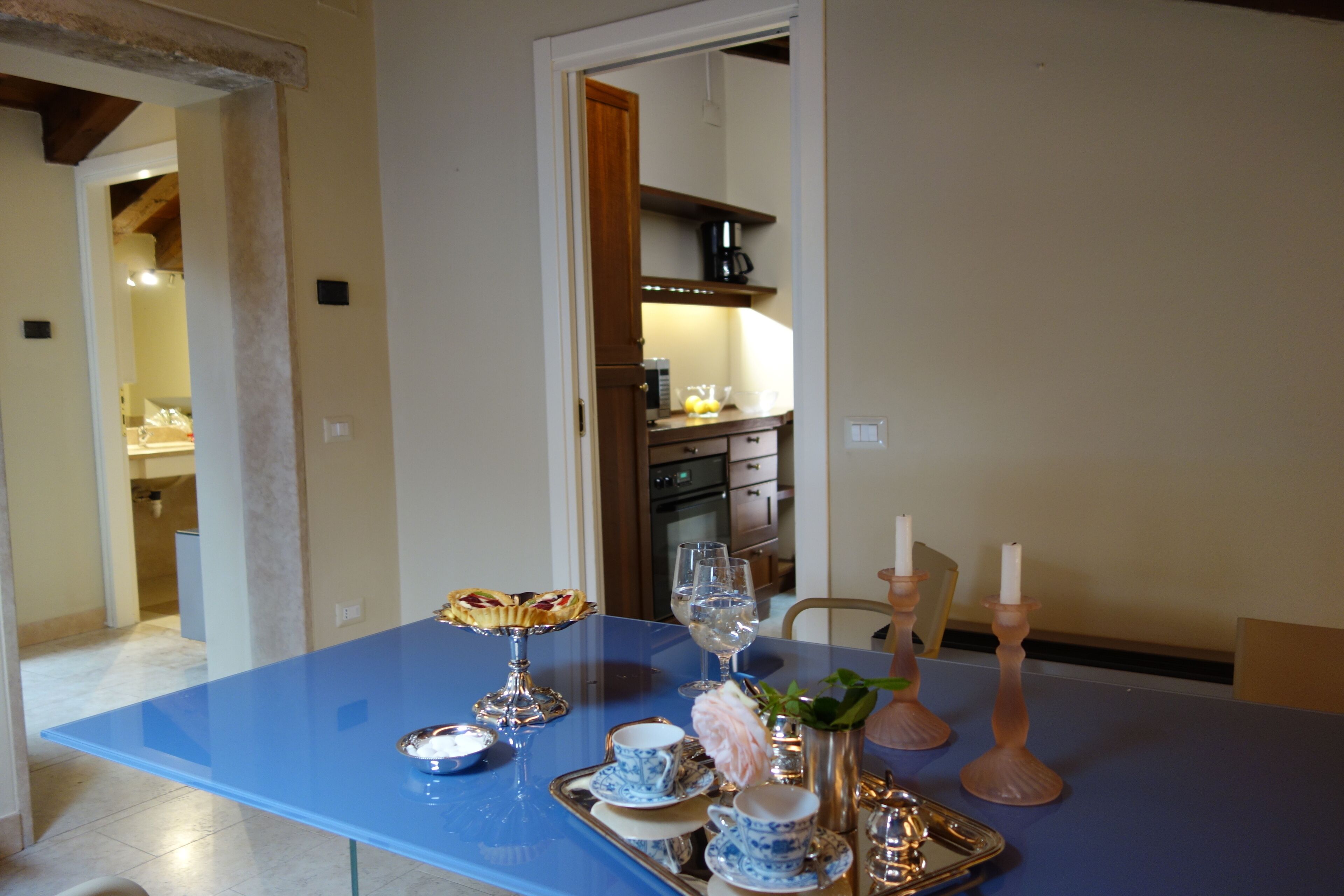 Una mesa de comedor con superficie azul, dispuesta con platos, vasos y un florero con flores.
