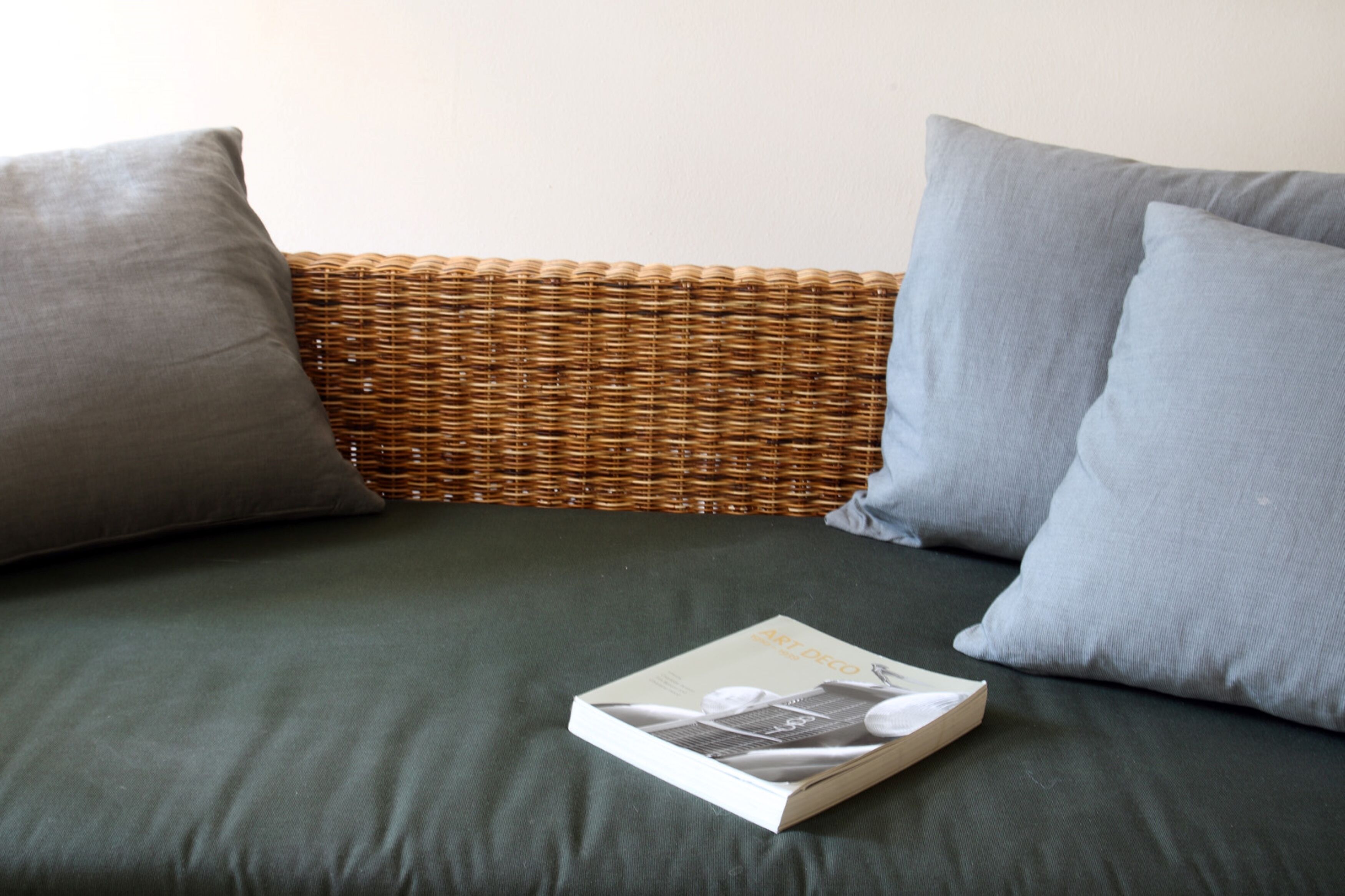 A wicker sofa with grey cushions and a book on it.