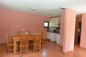 Ein Essbereich mit Holztisch und -stühlen, eine Küche mit weißen Schränken und einer Mikrowelle sowie eine rosa Wand.