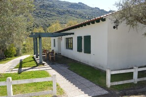 Ein weißes Gebäude mit grünen Fensterläden, einer Terrasse mit Stühlen und einem weißen Zaun.
