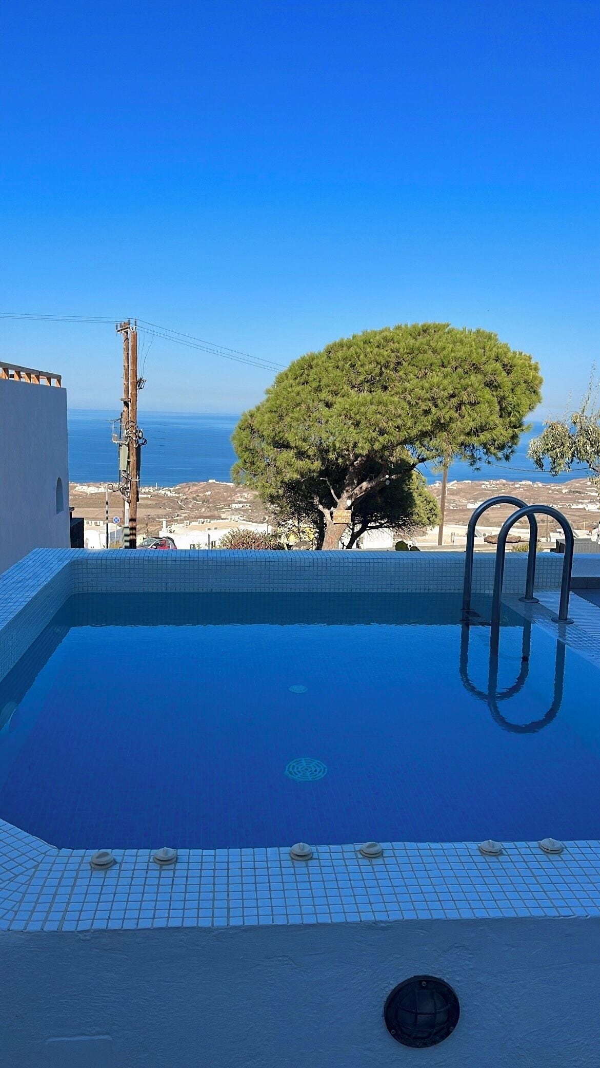 Uma piscina com água azul cristalina, borda azulejada e vista para o mar e a paisagem distante.