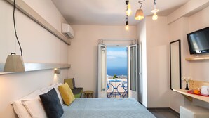 Una camera da letto con un letto, un comodino e una televisione. È presente un balcone con tavolo e sedie, e vista sul mare.