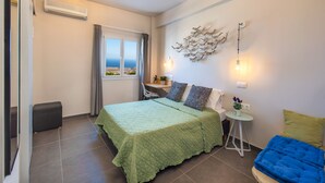 Una camera da letto con un letto, una scrivania, una sedia, un tavolino con una pianta e vista mare dalla finestra.