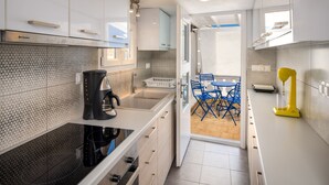 Una cucina funzionale con mobili bianchi, un piano cottura nero e una macchina da caffè. C'è un piccolo angolo ristoro con sedie blu e un tavolo.