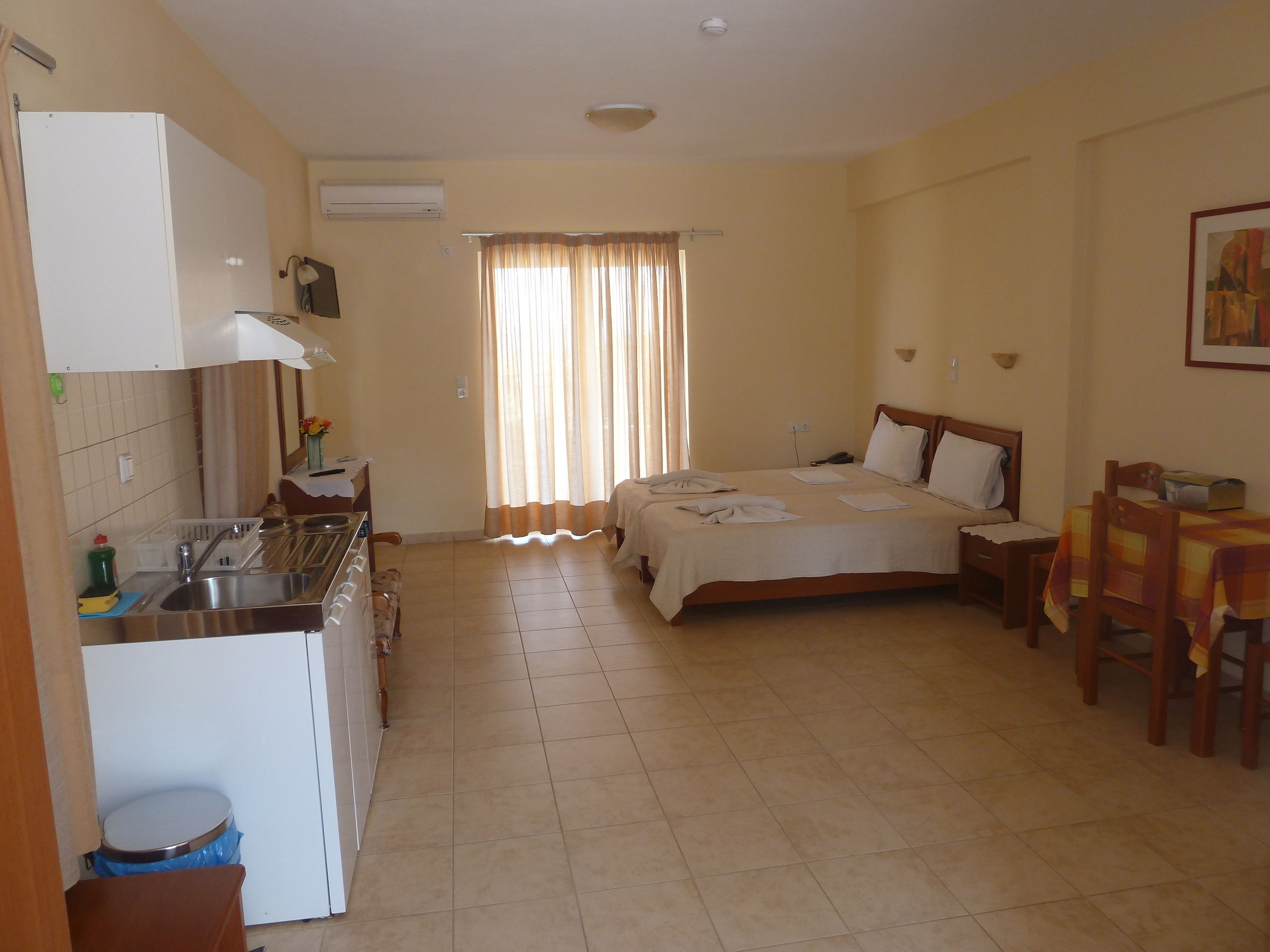 A hotel room with a kitchen area, a bed, a dining table, and a window with curtains.