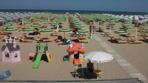 A beach with rows of umbrellas and sun loungers, a children's play area, and a clear view of the ocean. - Hotel Niagara Rimini (Rimini)