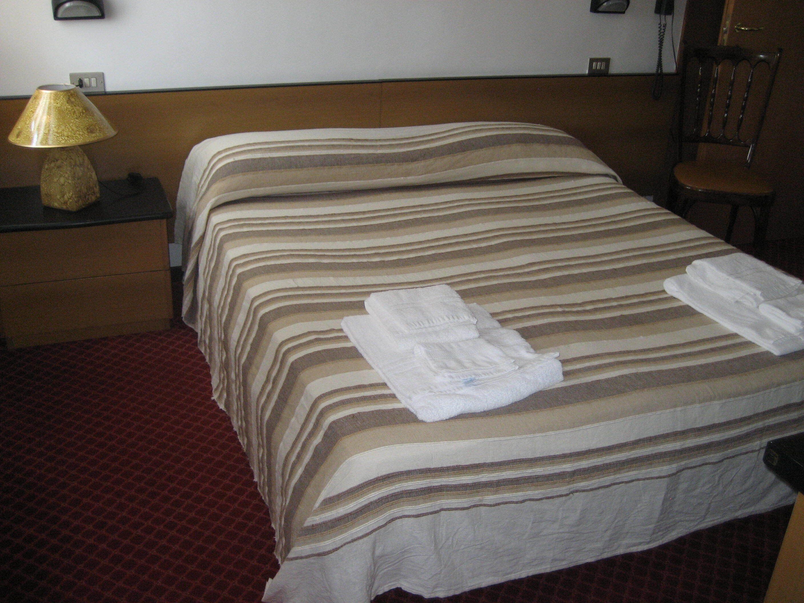 A hotel room with a bed, a nightstand, a lamp, and a chair.