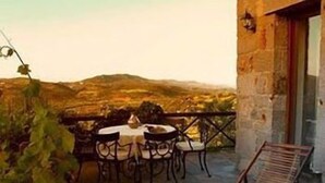 Edifici de pedra amb un pati que disposa d'una taula i cadires, amb vista a un paisatge amb muntanyes.