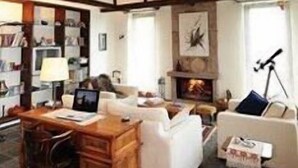 Un ampli saló amb viges de fusta a la vista, una llar de foc, un sofà, una taula de centre i una biblioteca.