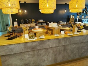 A buffet setup with various food items and utensils, including a jar of pickles and a bowl of soup.