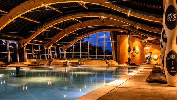 Una piscina interior con techos de madera arqueada y una gran escultura.