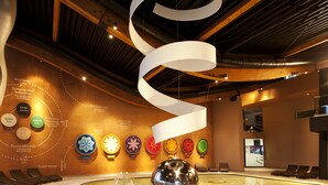 Un interior moderno con una escultura esférica central, zonas de estar y una pared que exhibe diversos artefactos culturales.