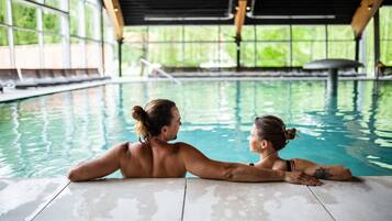 Una pareja se relaja junto a una piscina interior con vistas a la vegetación a través de amplios ventanales.