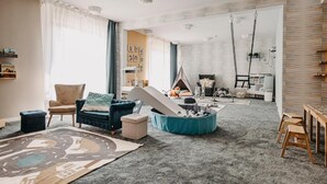 Una sala de estar acogedora con sofá, sillón y un asiento tipo saco azul. Hay una zona de juegos con un tobogán y una tienda tipi.