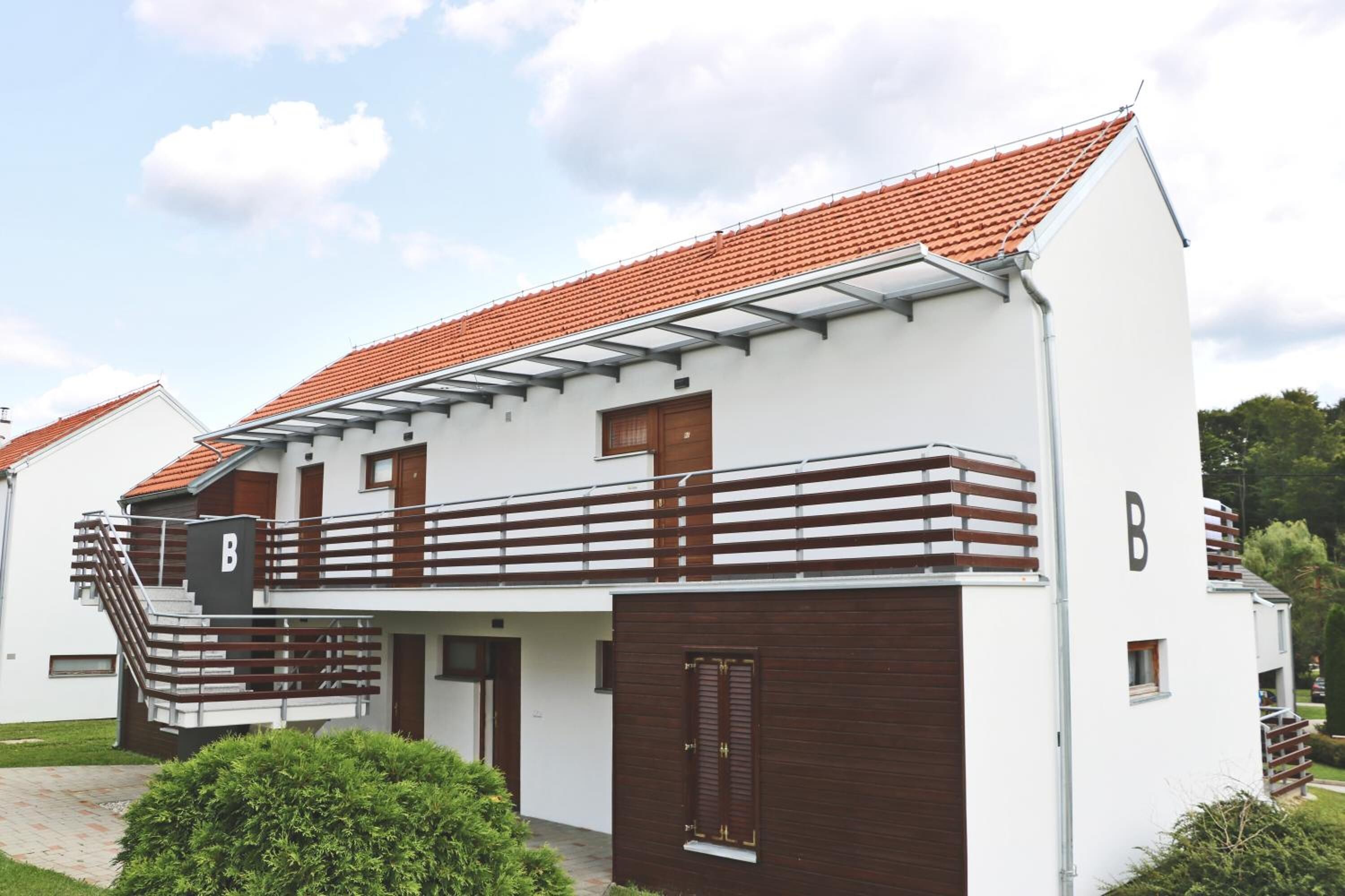 A modern two-story building with a red-tiled roof, a wooden balcony, and a 'B' sign indicating a business or office space.