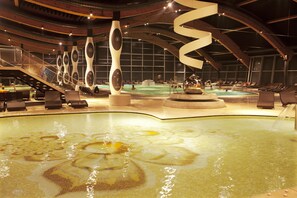 Un espace piscine intérieur moderne, agrémenté de sculptures originales, d’un élément aquatique central et d’un coin salon avec des chaises longues.