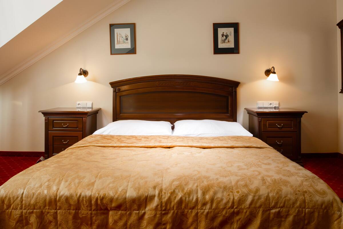A neatly made bed with a headboard, two bedside tables with lamps, and framed pictures on the wall.