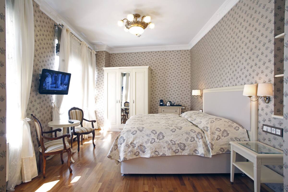 A hotel room with a bed, a television, a desk with a lamp, a chair, and a small table.