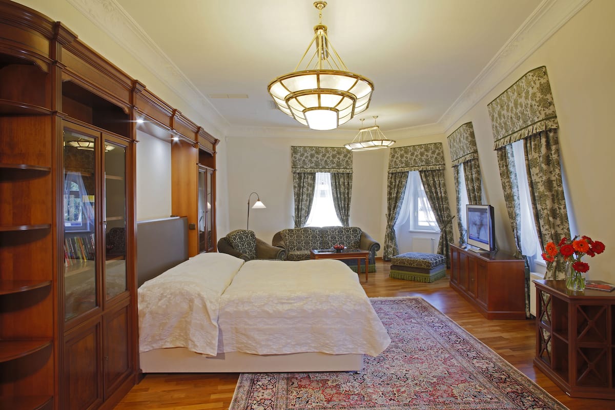 A spacious bedroom with a large bed, a wooden wardrobe, a television, and a floral-patterned window treatment.