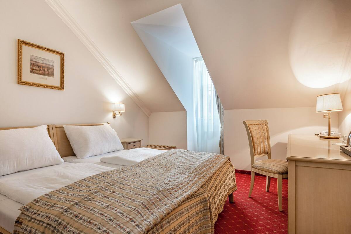A bedroom with a bed, a chair, a desk, and a window.