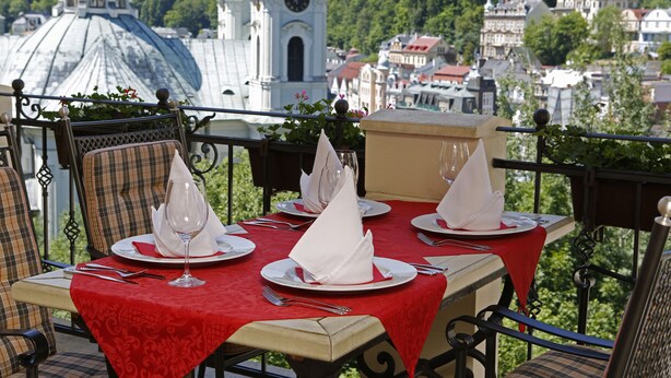 Ein Esstisch mit rotem Tischlein, weißen Servietten und Besteck, mit Blick auf eine Stadtlandschaft mit Kirche und Gebäuden.