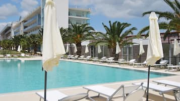 A swimming pool with lounge chairs and umbrellas, surrounded by palm trees and a modern building.