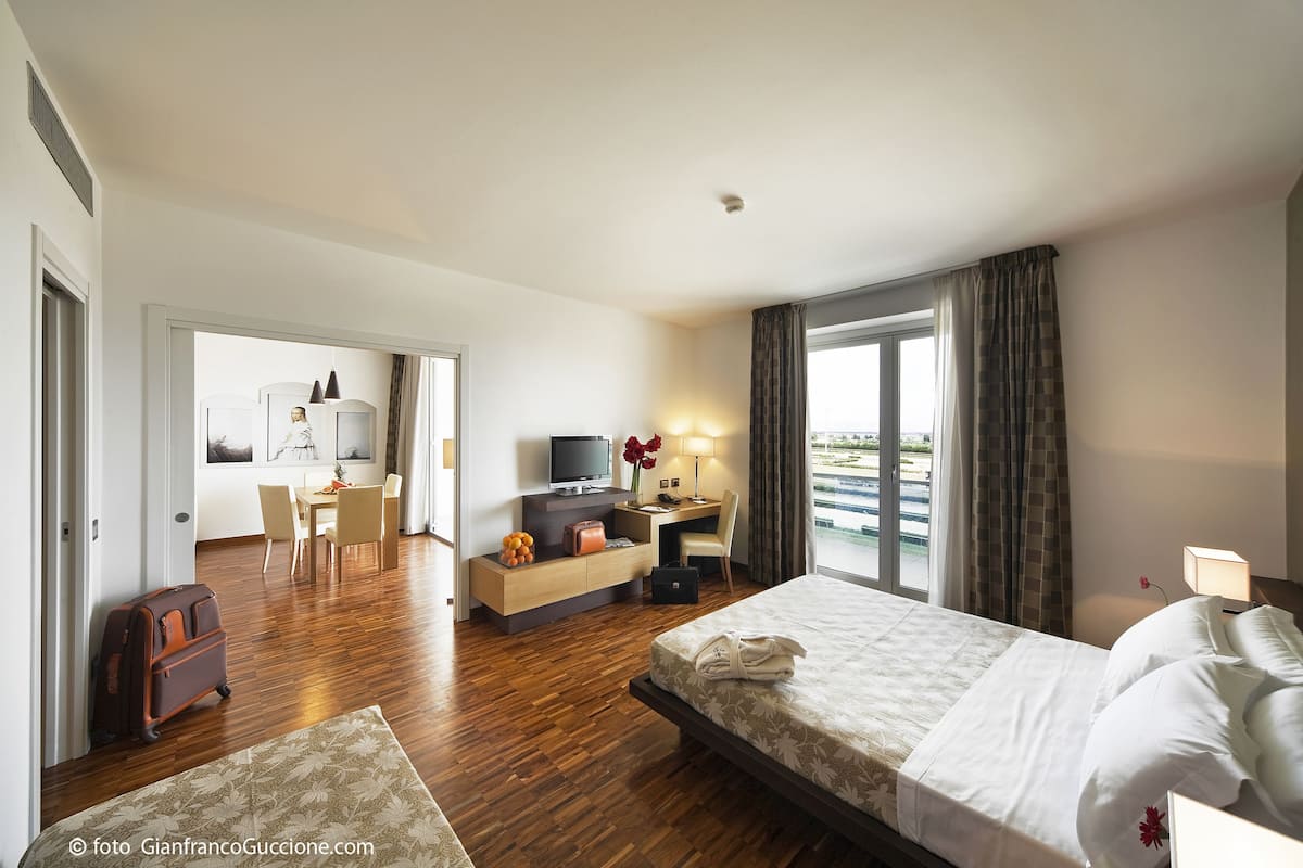 A hotel room with a bed, a desk, a chair, a TV, and a view of the outdoors.