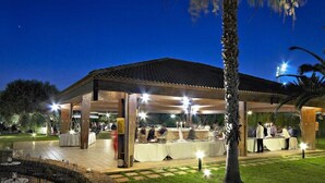 Un área de patio techada al aire libre con mesas y sillas, un muro de piedra y una palmera.