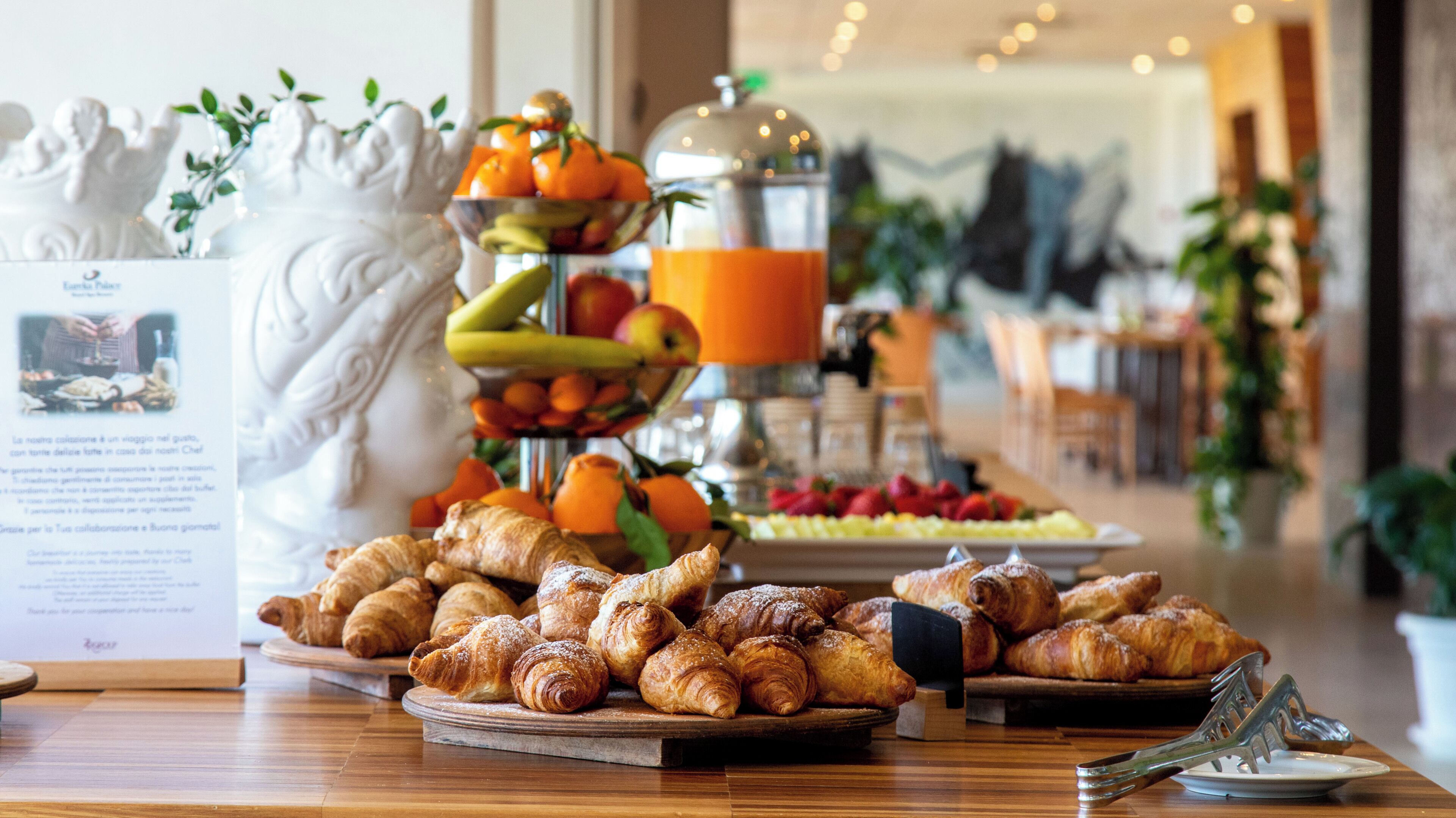 Un bufé de desayuno con bollería, frutas y un dispensador de zumo.
