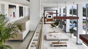 Un moderno vestíbulo de hotel con una larga recepción, varias zonas de estar y grandes ventanales con vistas al exterior.