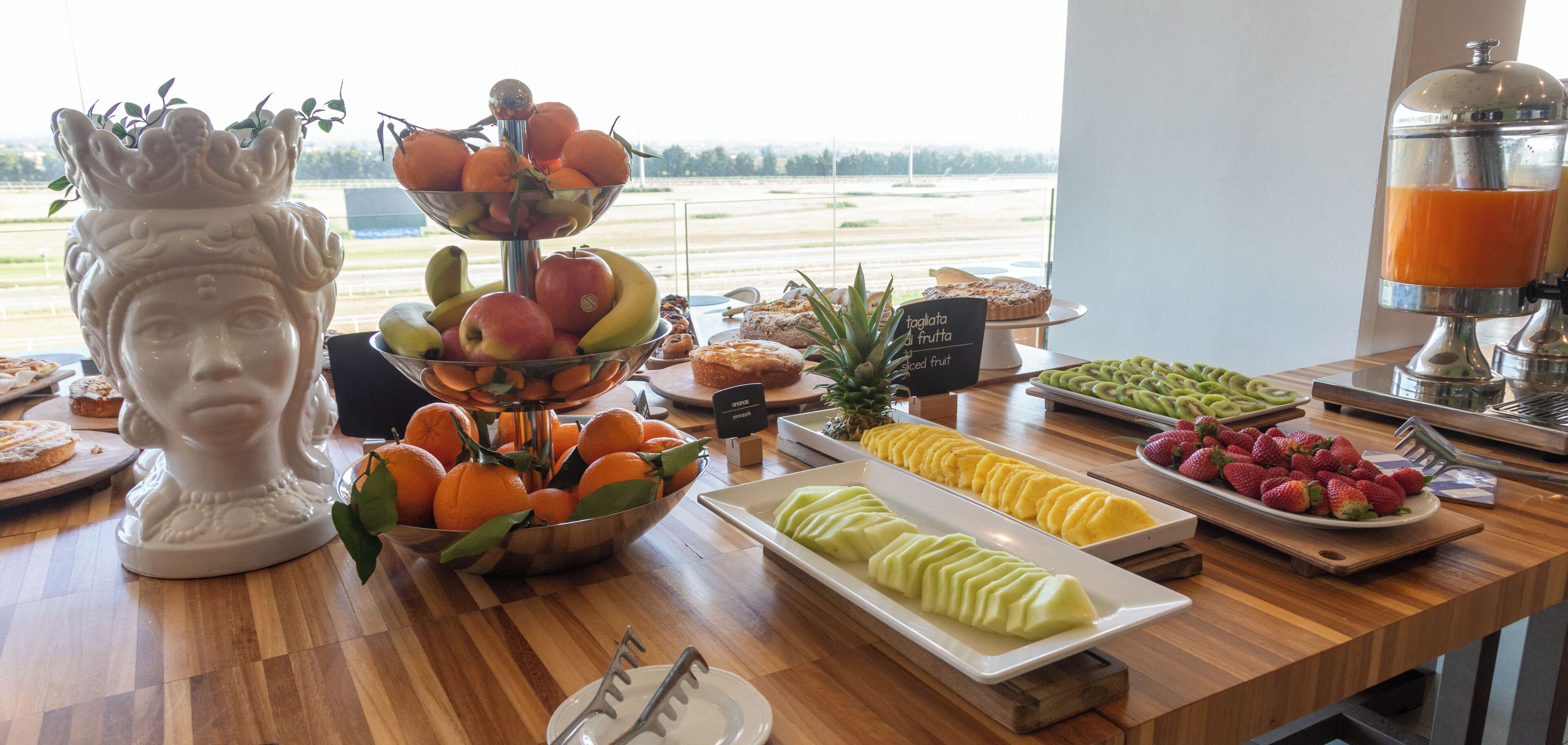 A buffet table with various fruits, pastries, and a fruit juicer.