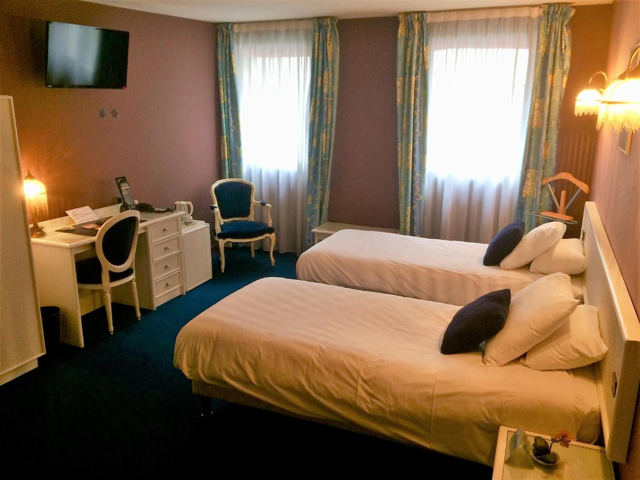 A hotel room with two beds, a desk with a chair, a television, and curtains.