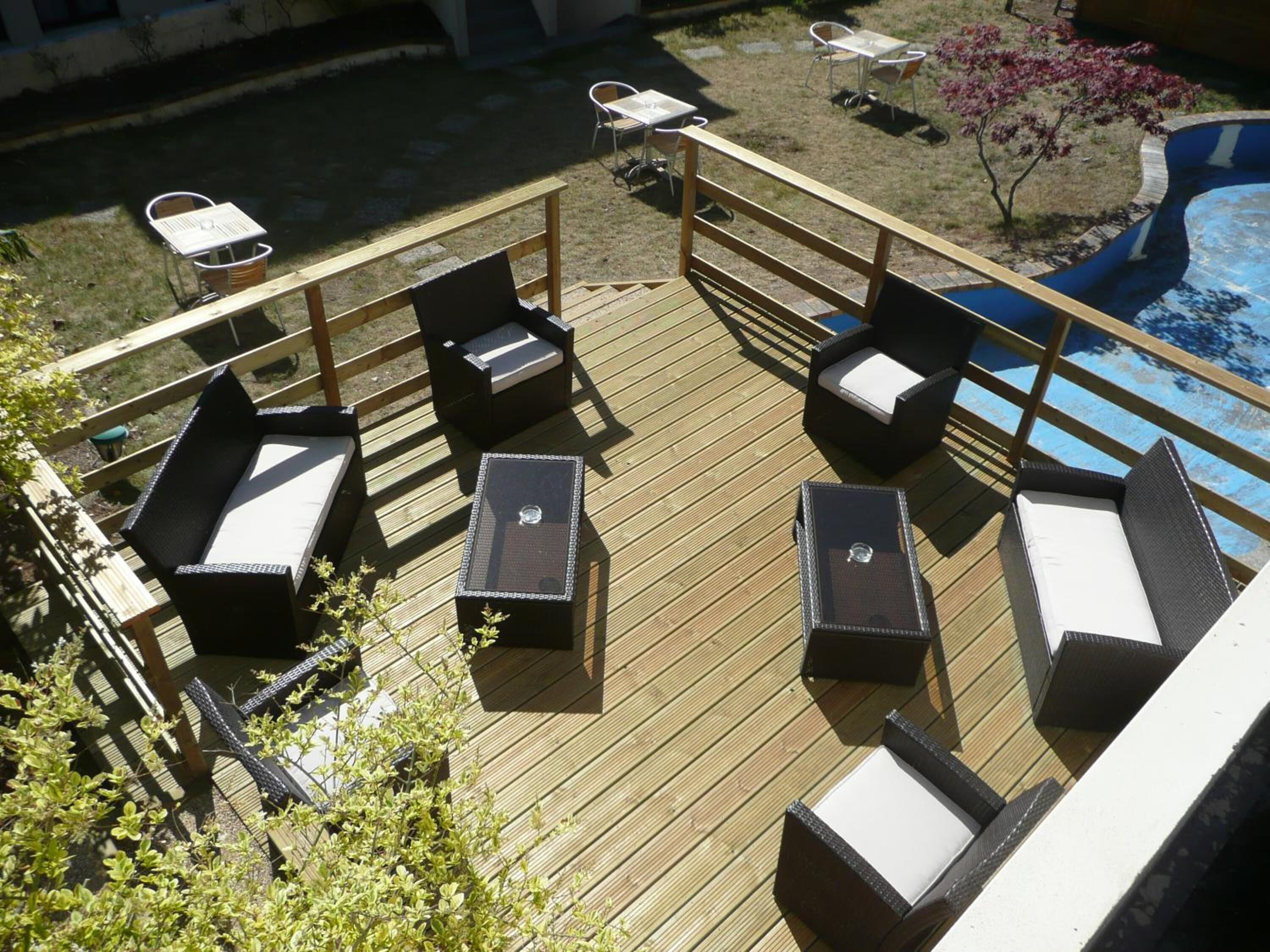 Une terrasse en bois avec des sièges d’extérieur, comprenant des chaises et des tables, et une piscine en arrière-plan.