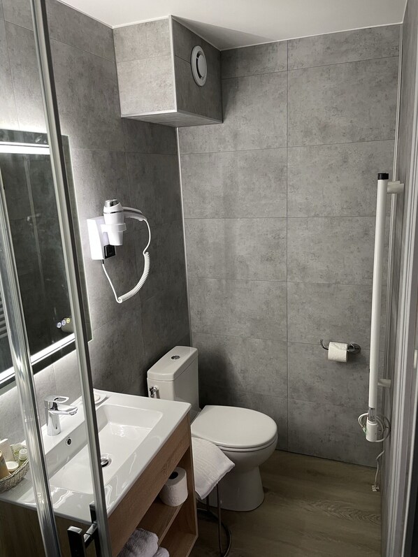 Un baño moderno con cabina de ducha de vidrio, un lavabo blanco y un inodoro.