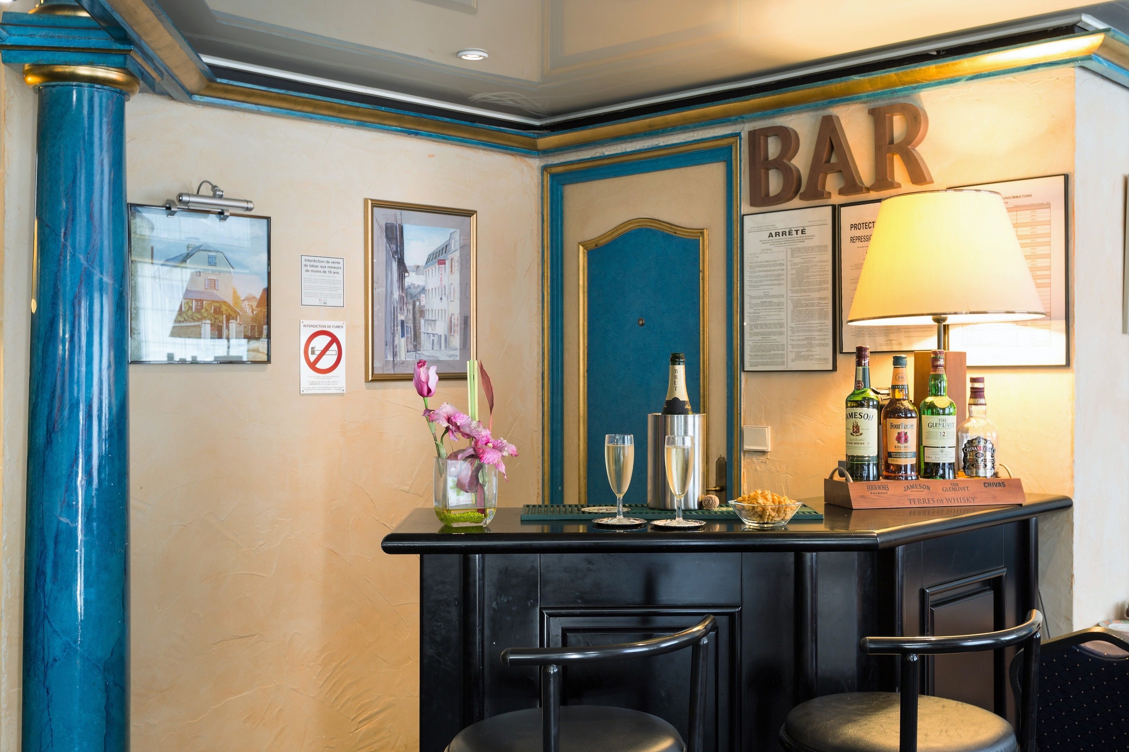 Een bar met een toonbank, barstoelen, een lamp en diverse flessen.